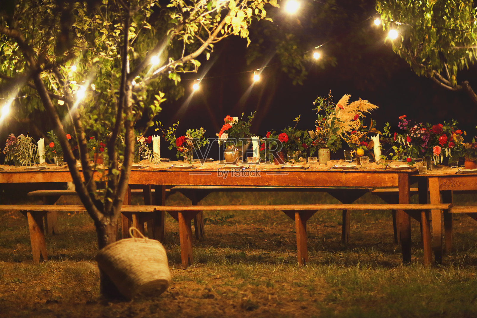 为一个乡村户外晚餐准备的桌子在晚上与葡萄酒杯，鲜花和灯照片摄影图片