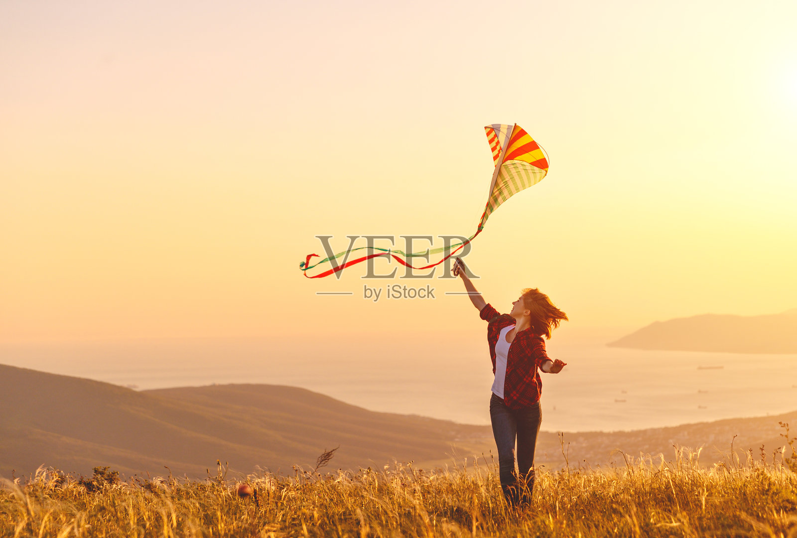 快乐的年轻女子与风筝跑在林间的日落在夏天照片摄影图片