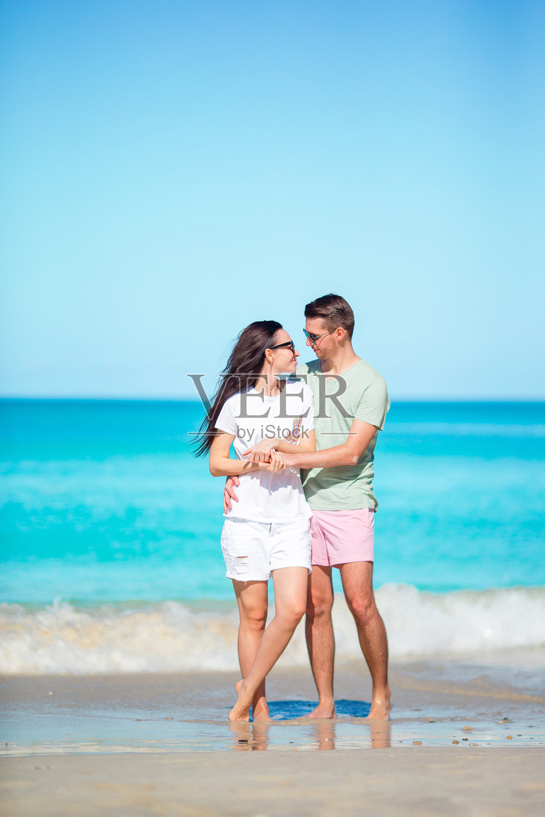 在加勒比海的安提瓜岛，一对年轻夫妇在白色沙滩和绿松石海水的热带海滩上散步照片摄影图片