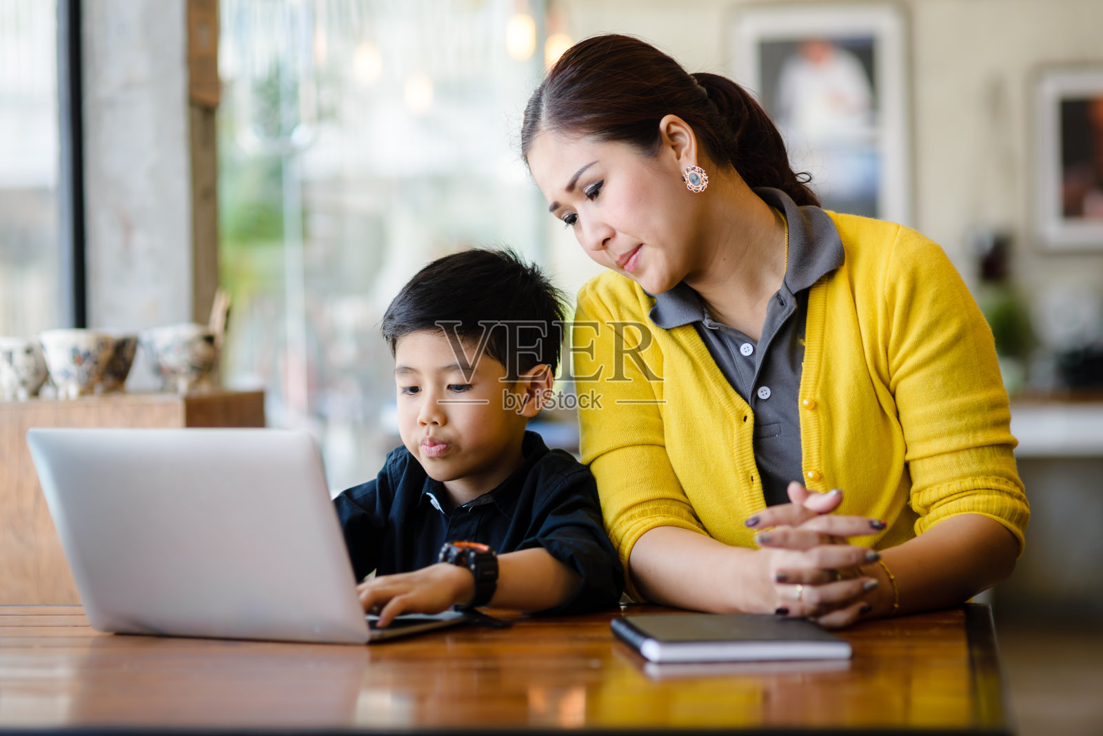 快乐的亚洲母亲和她的儿子在家里使用笔记本电脑。照片摄影图片