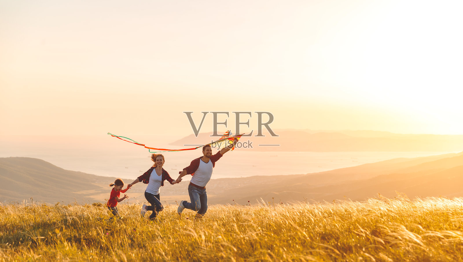幸福的家庭，父亲，母亲和孩子的女儿在大自然放风筝在日落照片摄影图片