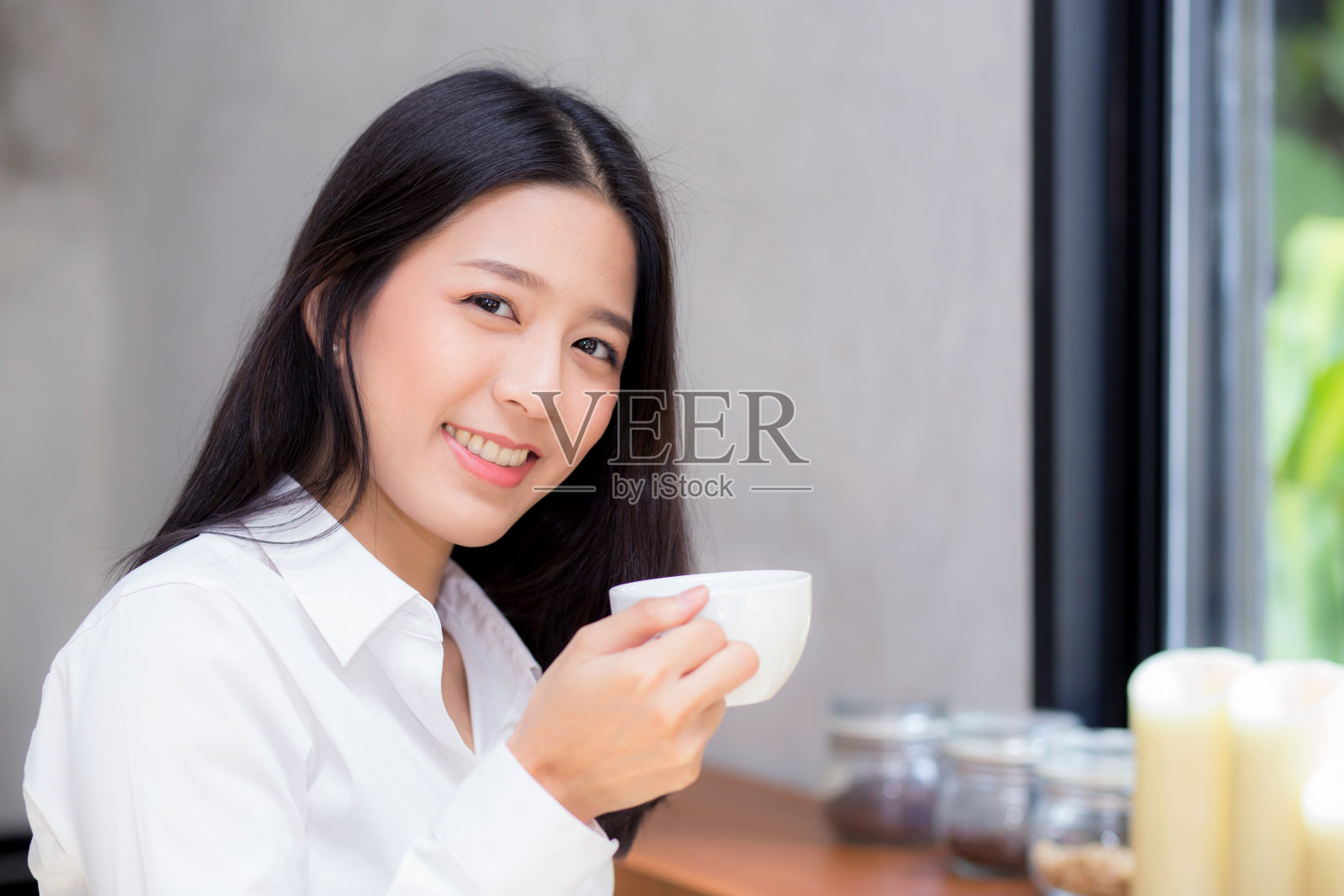 美丽的年轻亚洲女人喝咖啡和微笑在早上的咖啡馆，女孩坐在咖啡店吃早餐和休闲在空闲时间。照片摄影图片