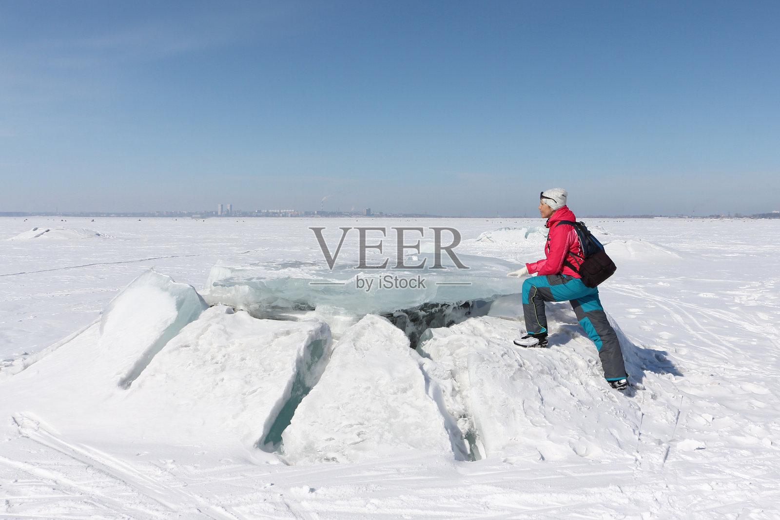俄罗斯Ob水库，穿着红色夹克的快乐女人踩在冰冻河流的浮冰上照片摄影图片