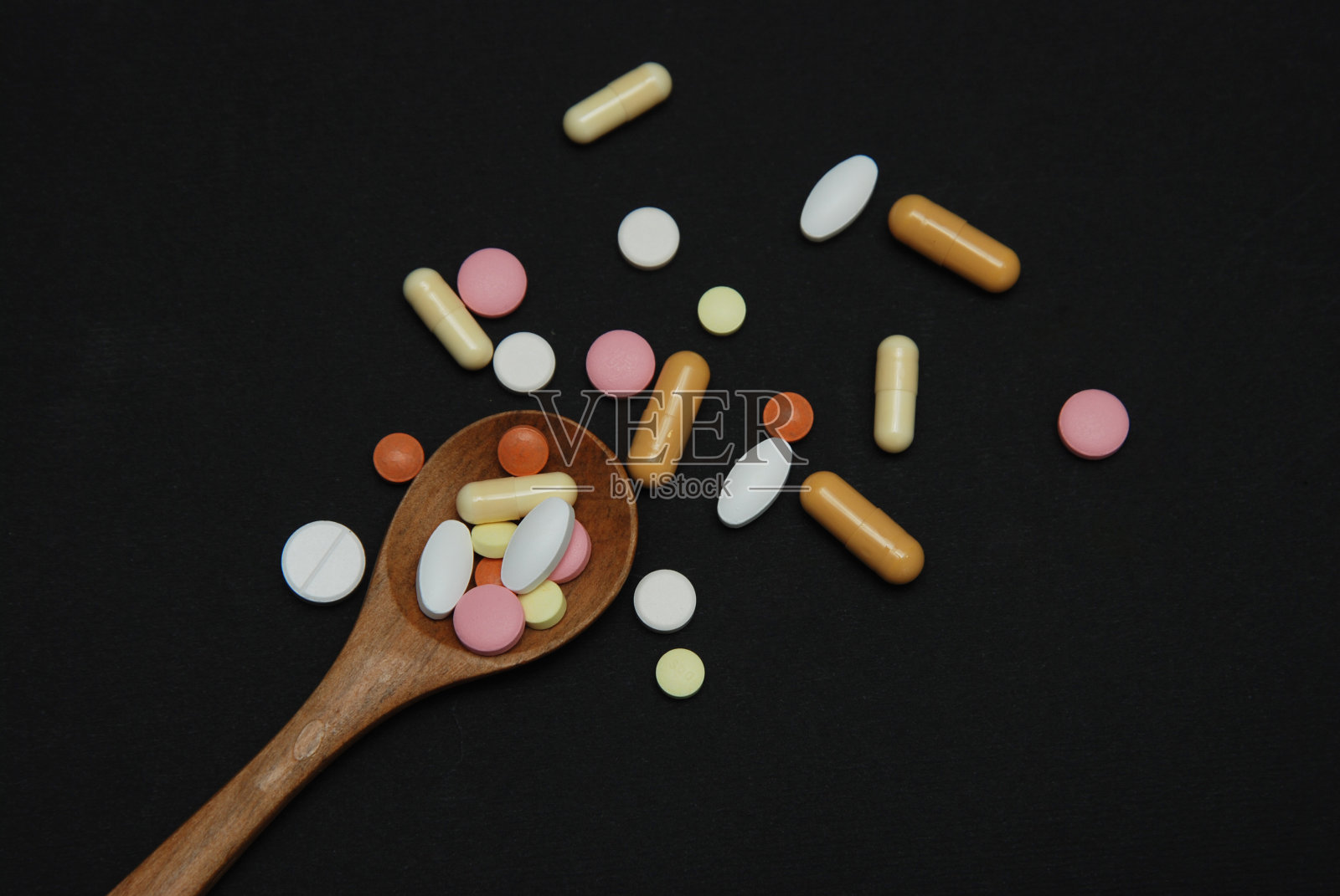 彩色药丸在木勺与部分药药丸孤立在黑色背景。健康和医学概念。照片摄影图片
