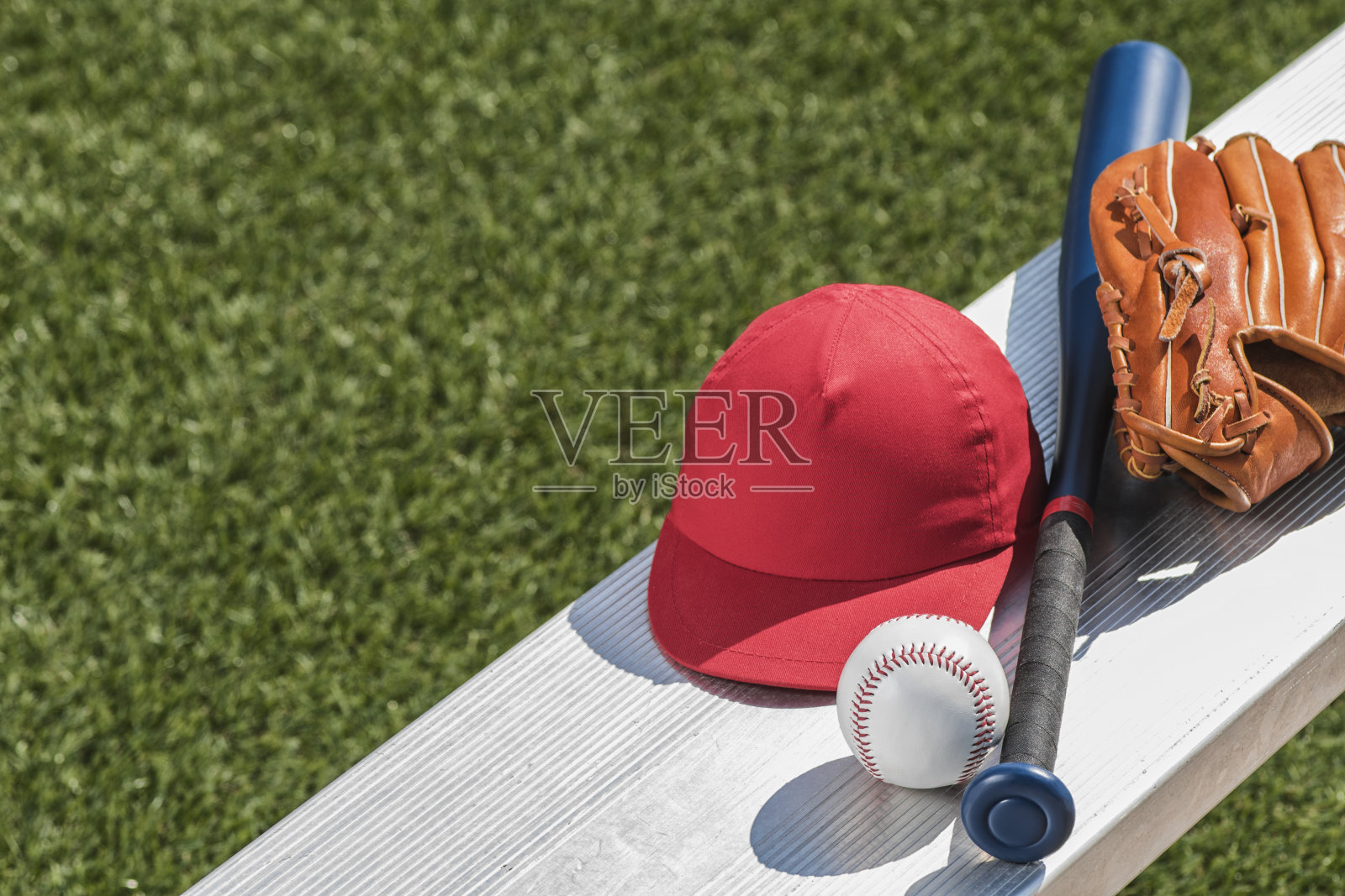 一个棒球，一顶红帽子，一副棒球手套和板凳上的球棒照片摄影图片