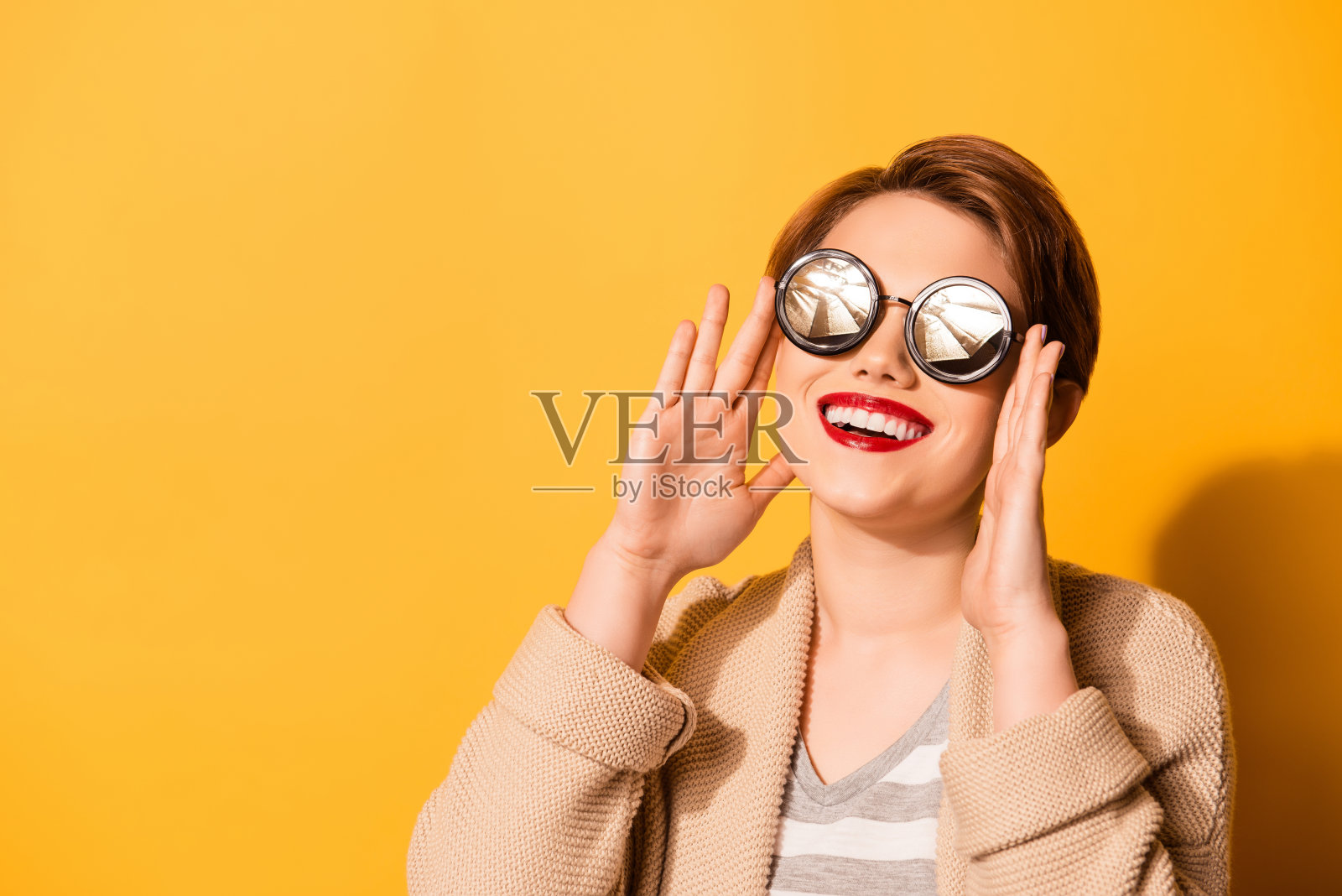 一个可爱的女孩，带着可爱的微笑，戴着时尚的太阳镜，穿着休闲的衣服在明亮的黄色背景照片摄影图片