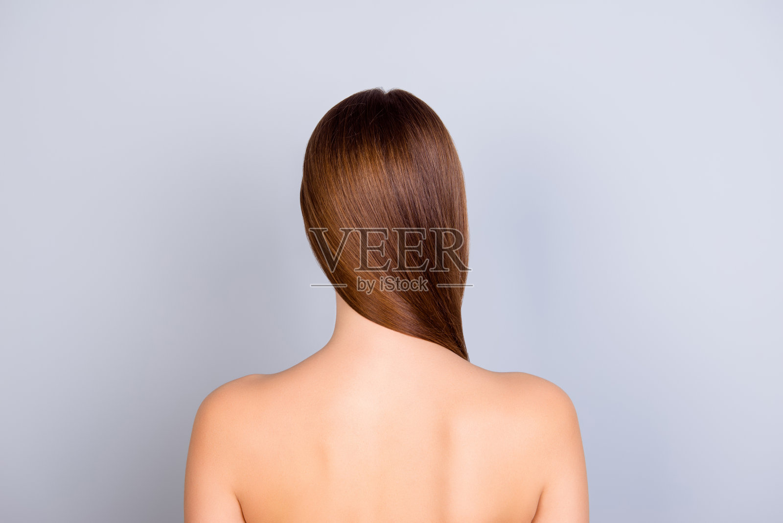 近裁剪的背影照片，年轻的棕色头发的女孩站在浅蓝色的背景。她有健康光亮的皮肤和头发照片摄影图片