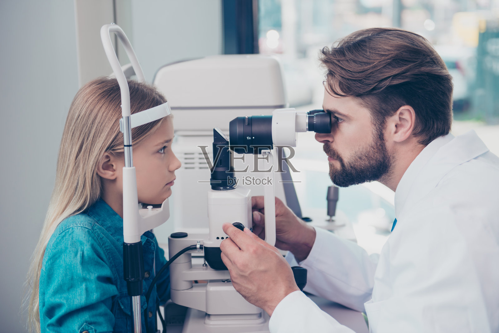 医疗、医药、视力和科技理念。在眼科诊所，聚焦深色胡子的验光师正在用非接触式眼压计检查小金发女孩的眼压照片摄影图片