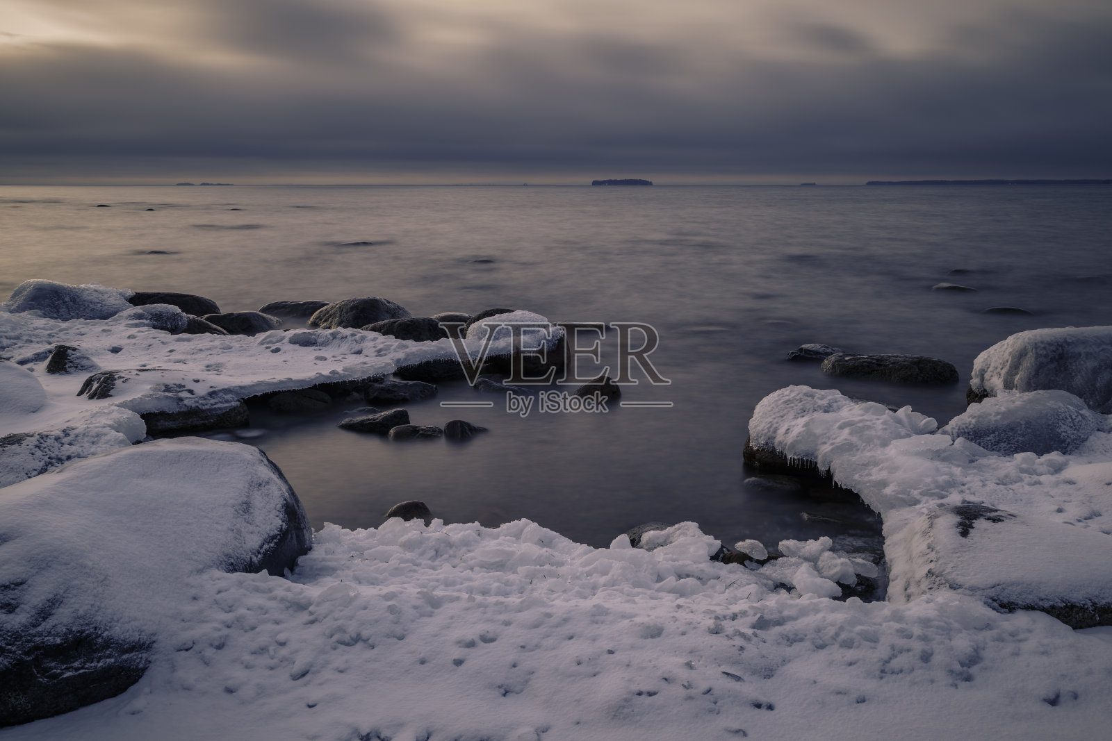 美丽的日落时分，冰雪覆盖在海岸边的岩石上照片摄影图片