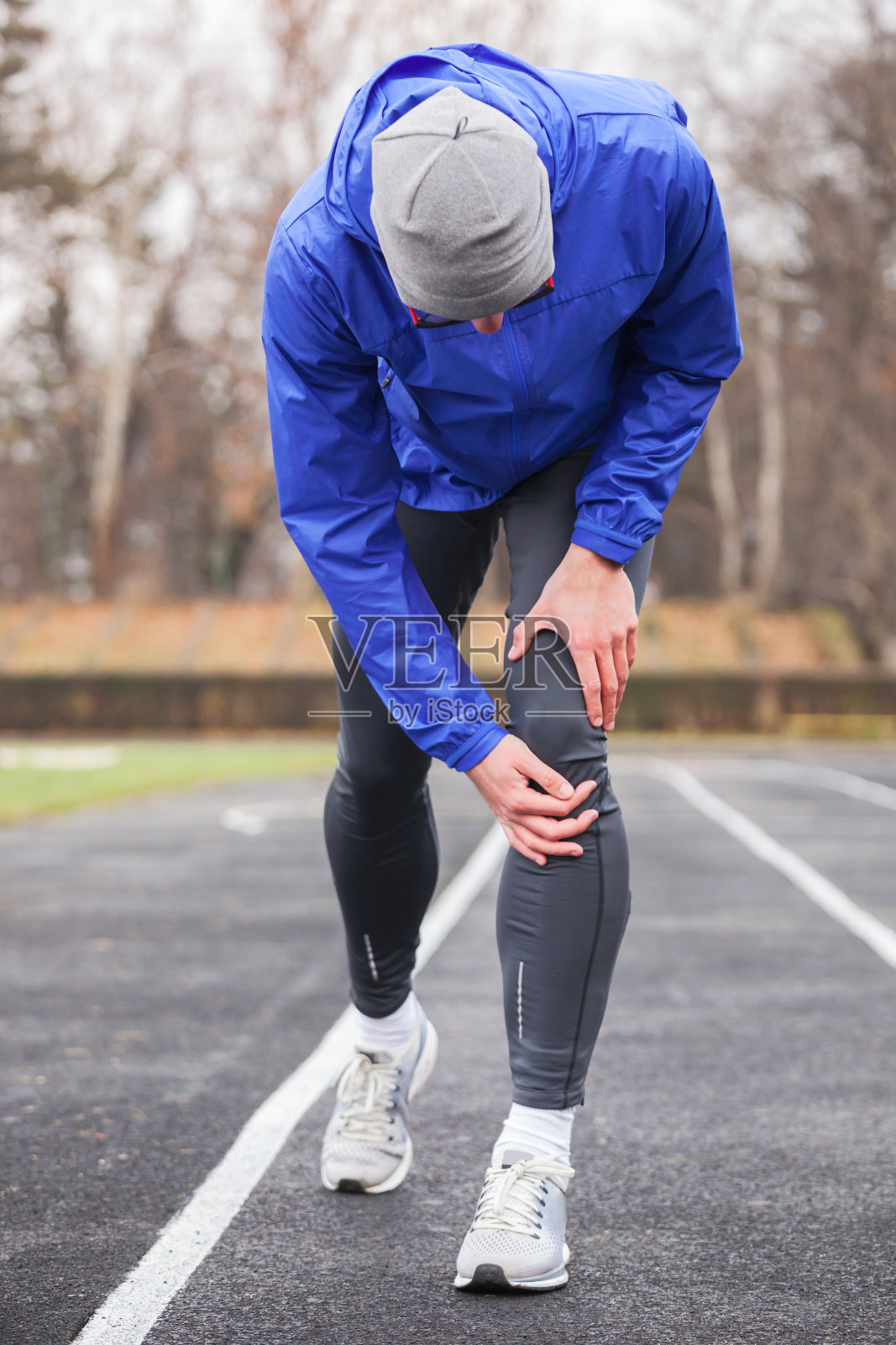 一个年轻的跑步者在跑步时抱着受伤的膝盖。照片摄影图片