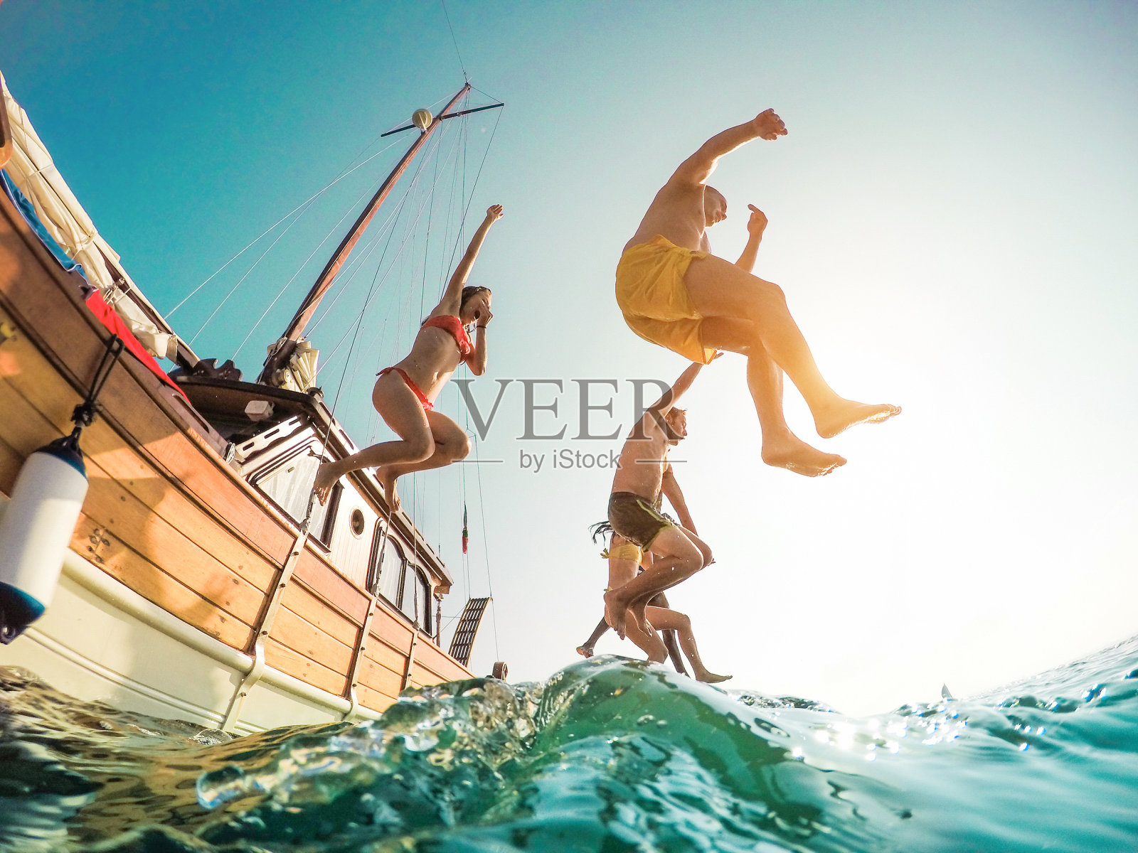 快乐的朋友从帆船跳入大海-年轻人在夏天的远足日在海洋里跳-度假，青春和乐趣的概念-主要集中在左边的人-鱼眼镜头扭曲照片摄影图片