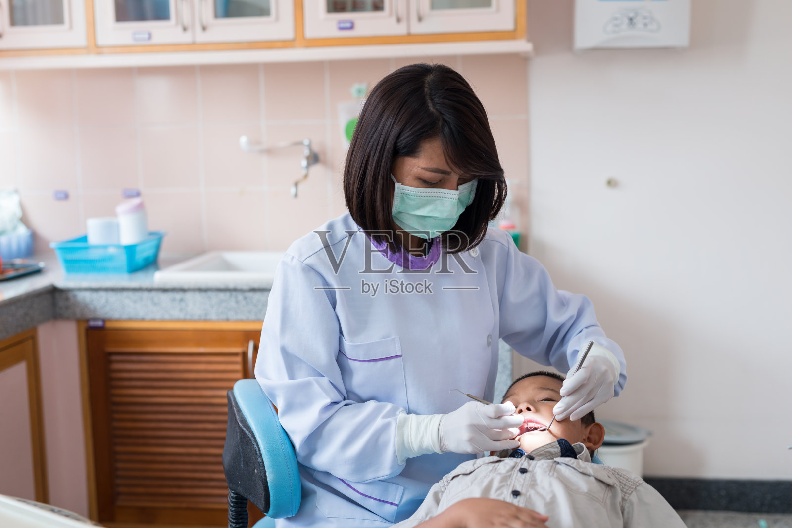 牙医拿着牙科工具。在医院给躺在牙科椅上的男孩检查牙齿。照片摄影图片