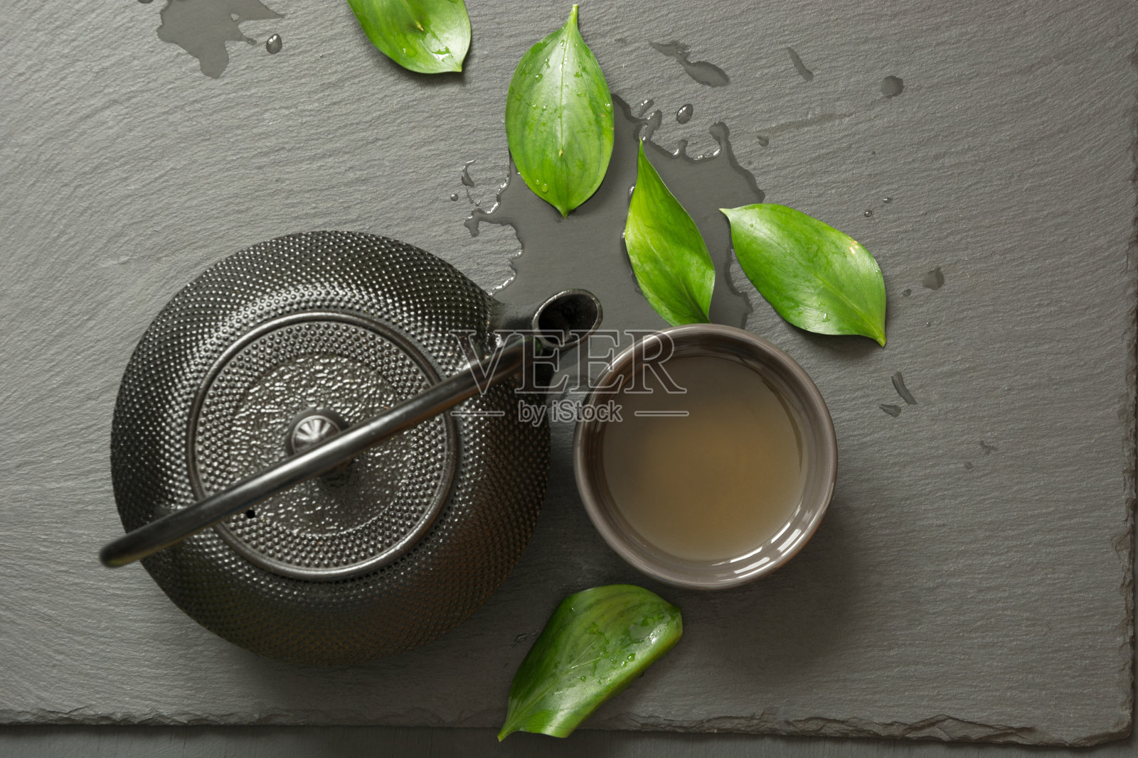黑石板背景上的日本绿茶。黑色茶壶和碗与绿茶。俯视图，复制空间。照片摄影图片
