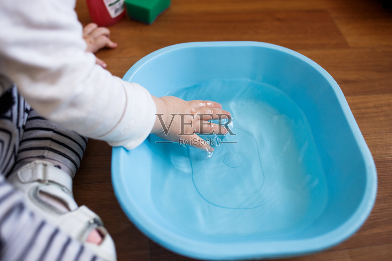 蹒跚学步的孩子把手放在地板上的一个蓝色的盆里照片摄影图片