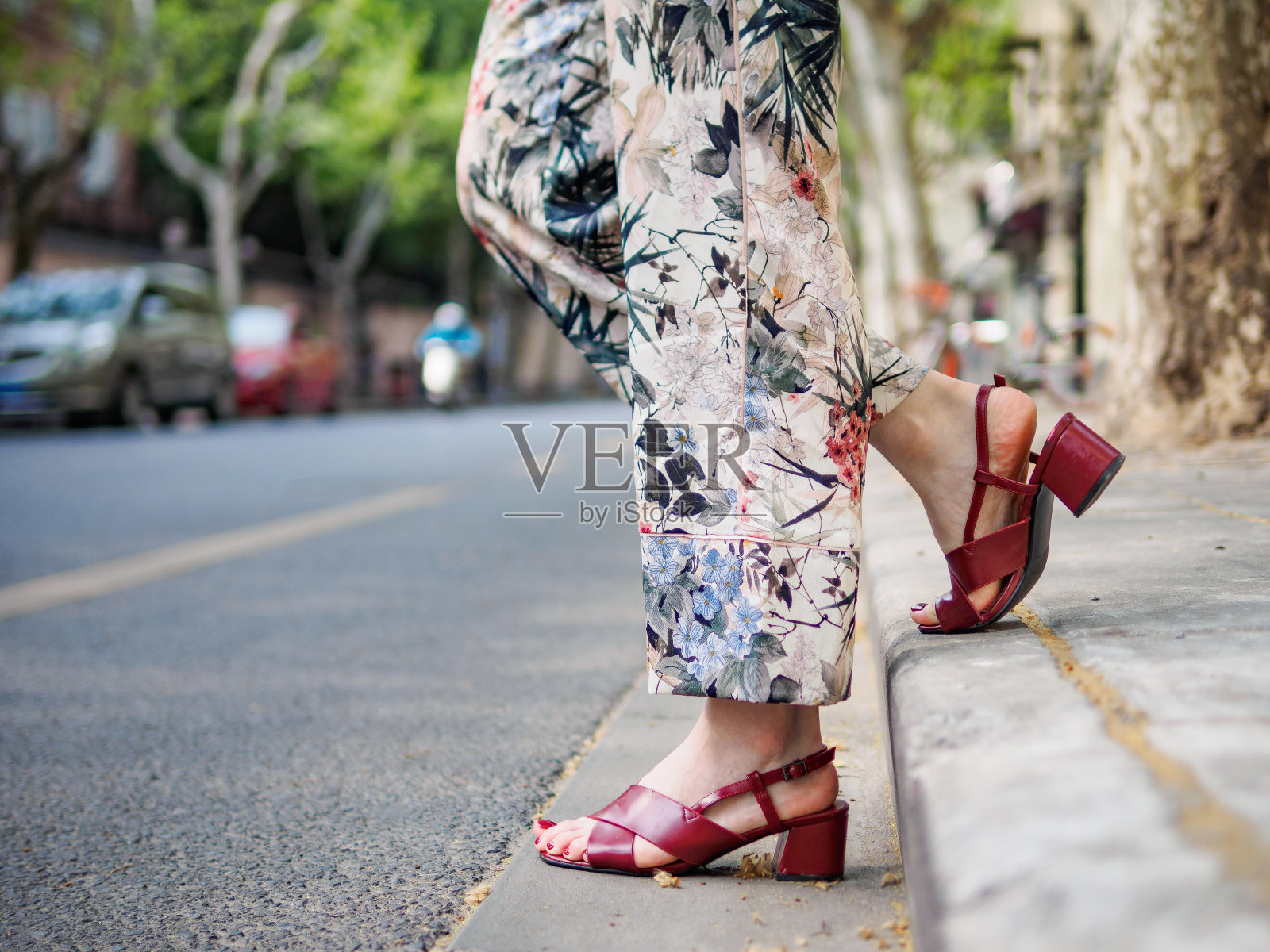 近距离拍摄女孩脚上穿着红色凉鞋的城市，以城市道路为背景。照片摄影图片