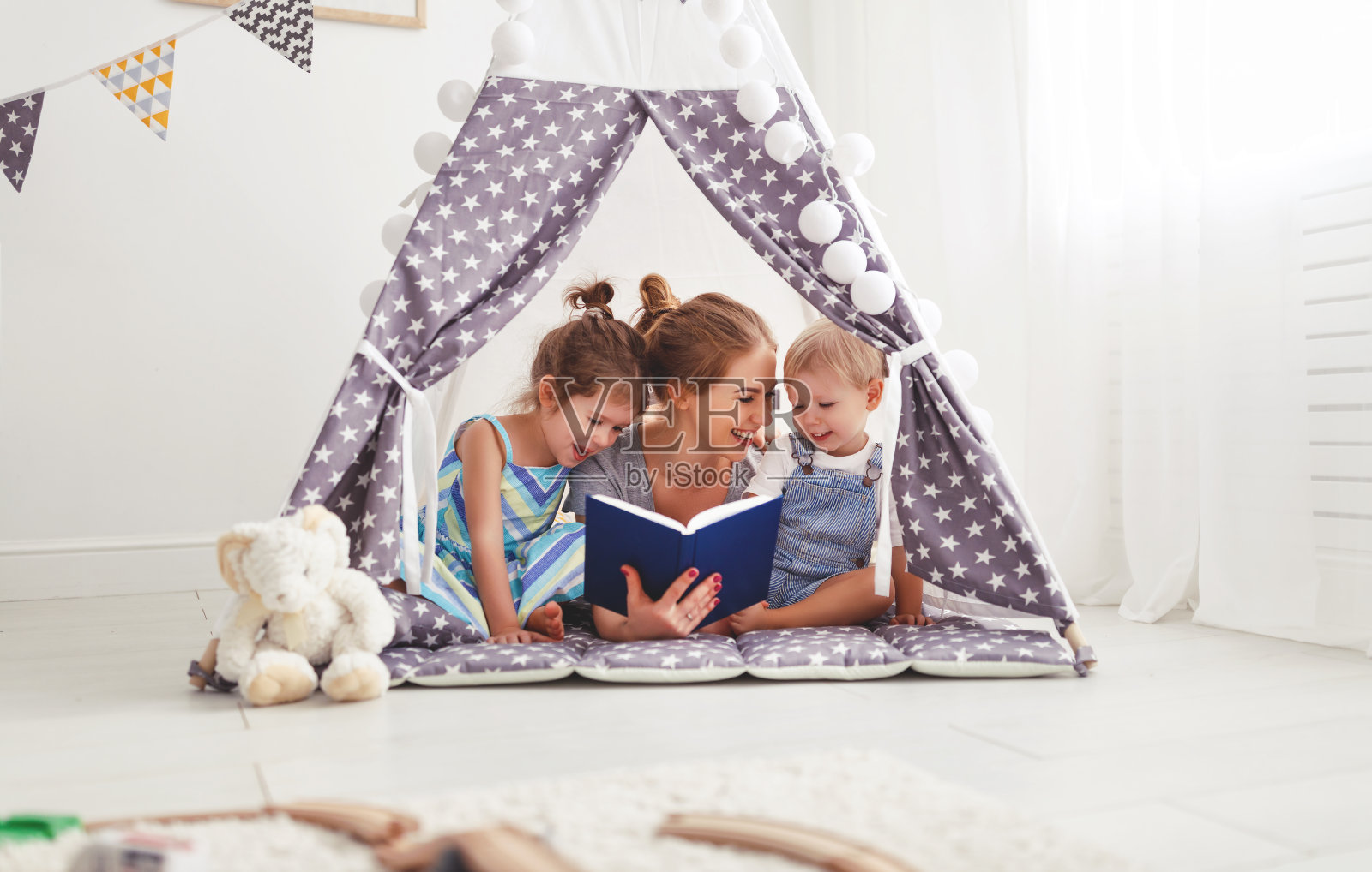 家庭母亲在家里的帐篷里给孩子读书照片摄影图片