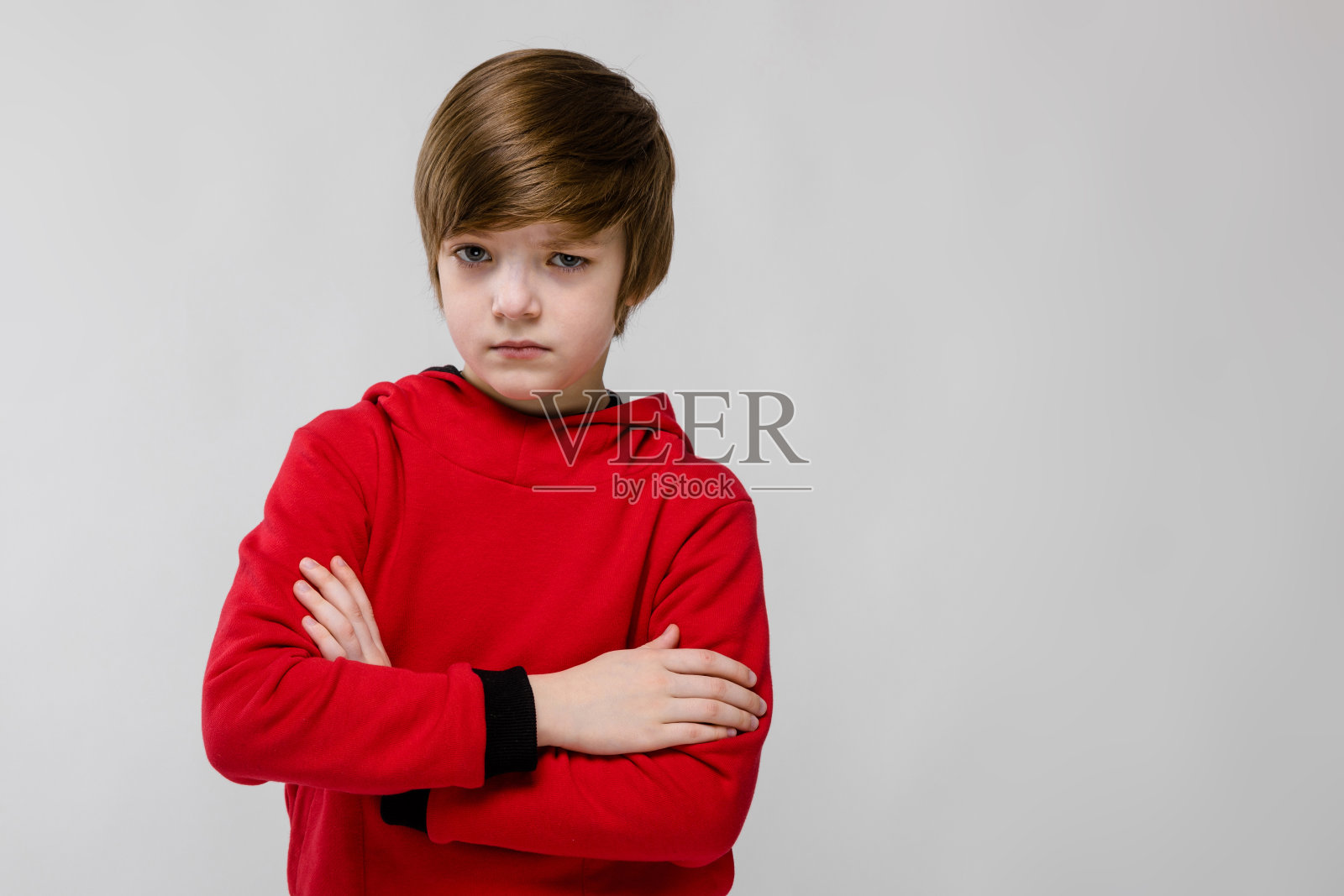 可爱自信严肃的白种人小男孩在红色毛衣与交叉的胳膊在灰色的背景照片摄影图片