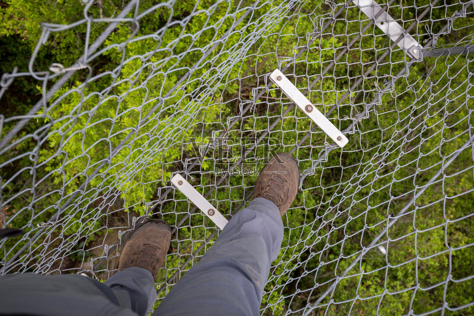 一个穿着灰色裤子的徒步旅行者穿过河上岩石上的吊桥的观点照片摄影图片