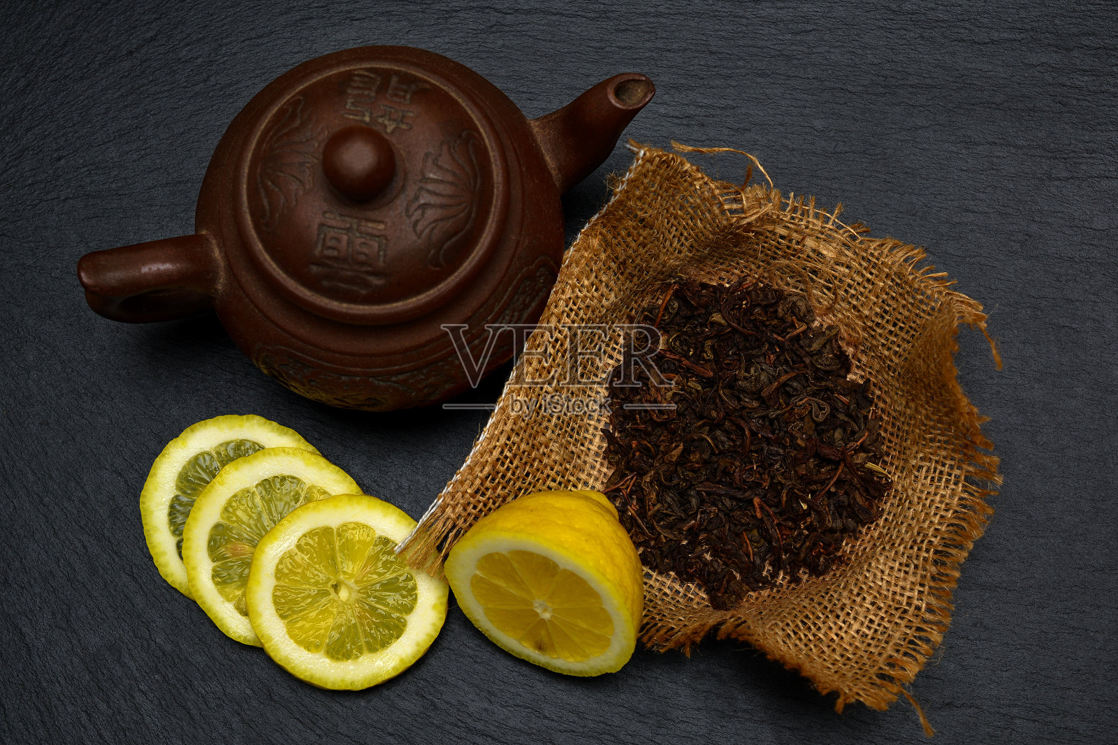 茶壶，熟透柠檬的一半和片，干茶叶放在黑板，盘子或托盘。照片摄影图片