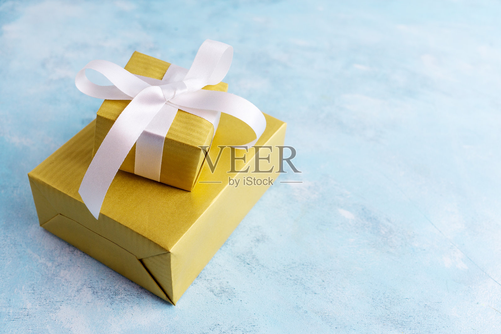 两个礼品盒在金色的纸与白色蝴蝶结在蓝色的背景。节日的概念。新年，圣诞节，生日礼物。文本空间照片摄影图片
