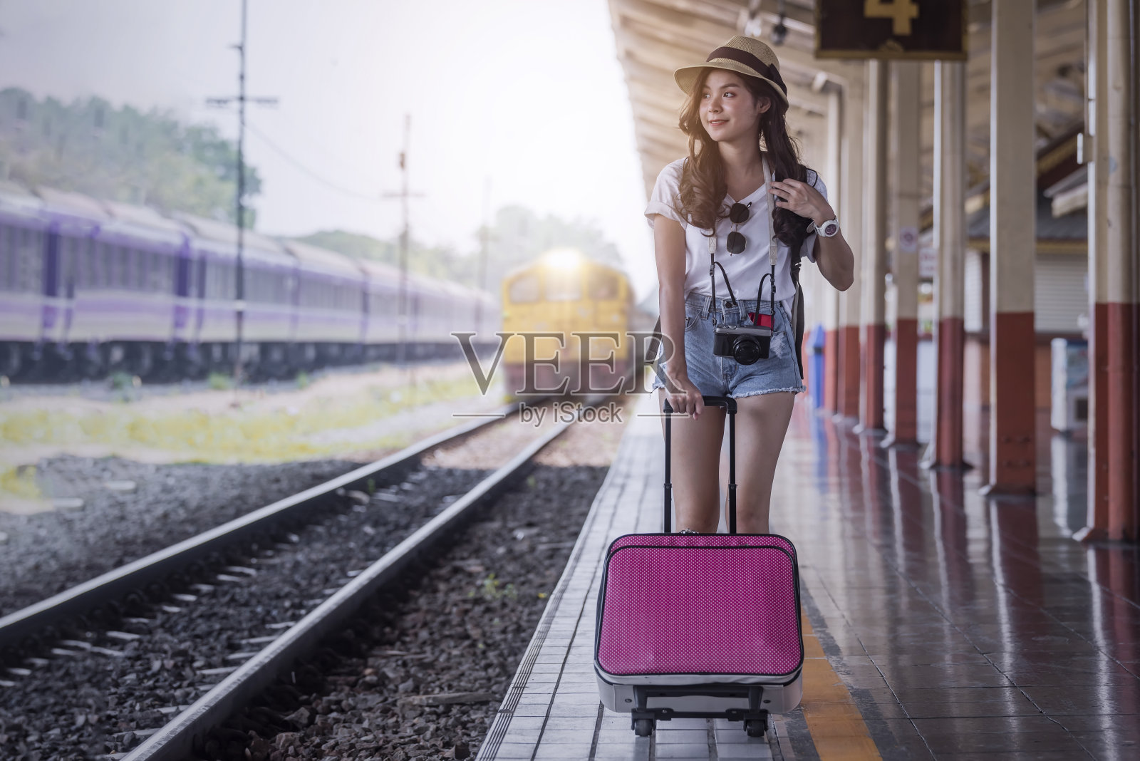 年轻漂亮的女人带着粉红色的行李走在火车站的月台上照片摄影图片