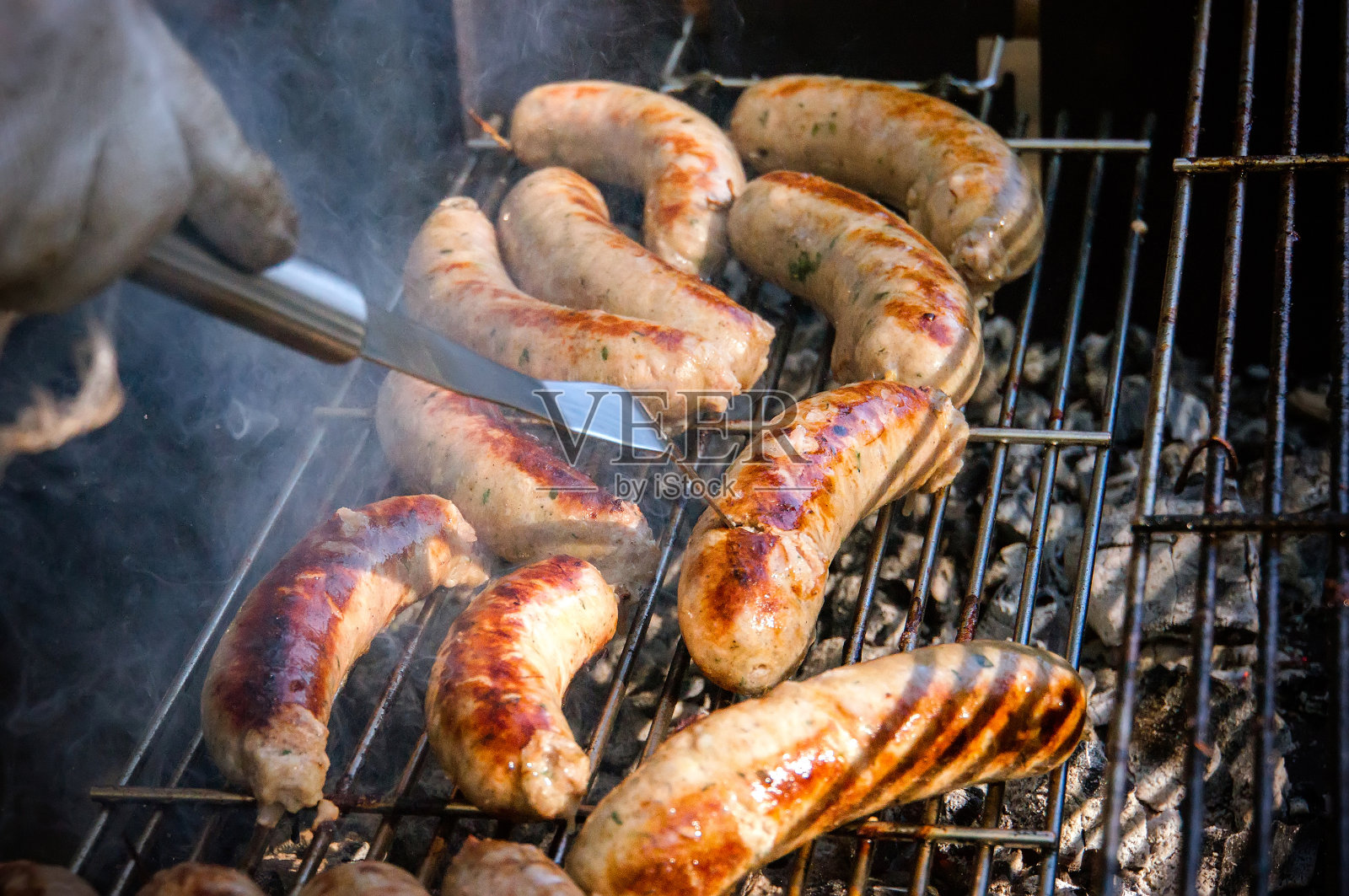 新鲜的香肠和热狗在户外燃气烧烤架上烧烤。照片摄影图片