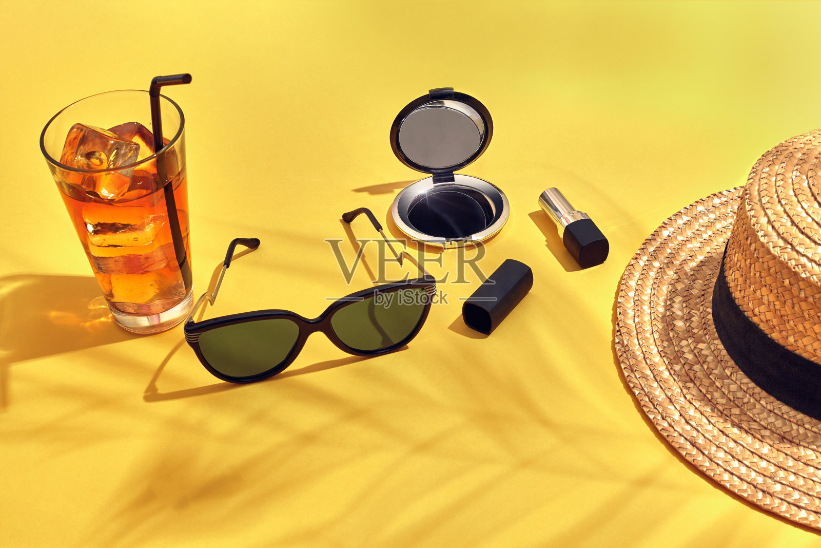 草海滩妇女的帽子，饮料与冰在一个玻璃杯和太阳眼镜在黄色的背景与棕榈叶的阴影照片摄影图片