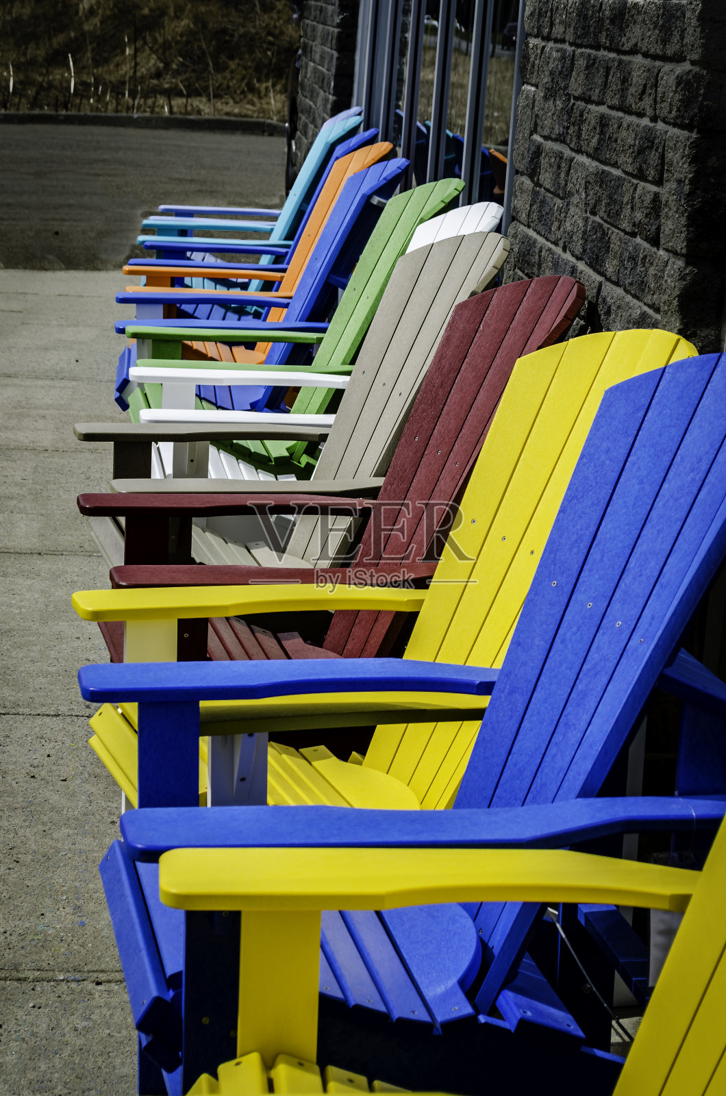 一排空的彩色阿迪朗达克椅子靠着灰色的砖墙和人行道上的店面窗户照片摄影图片