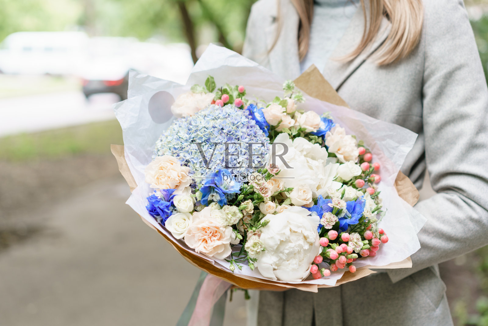 年轻的女孩拿着美丽的春天的花束。以绣球花和牡丹插花。颜色浅蓝色。花店的概念，一个小型家庭企业照片摄影图片