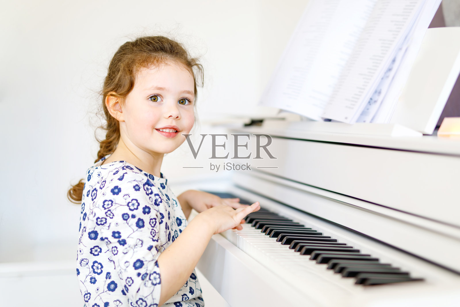 可爱健康的小女孩在客厅或音乐学校弹钢琴。学龄儿童在学习乐器的过程中获得乐趣。教育、技能的概念照片摄影图片