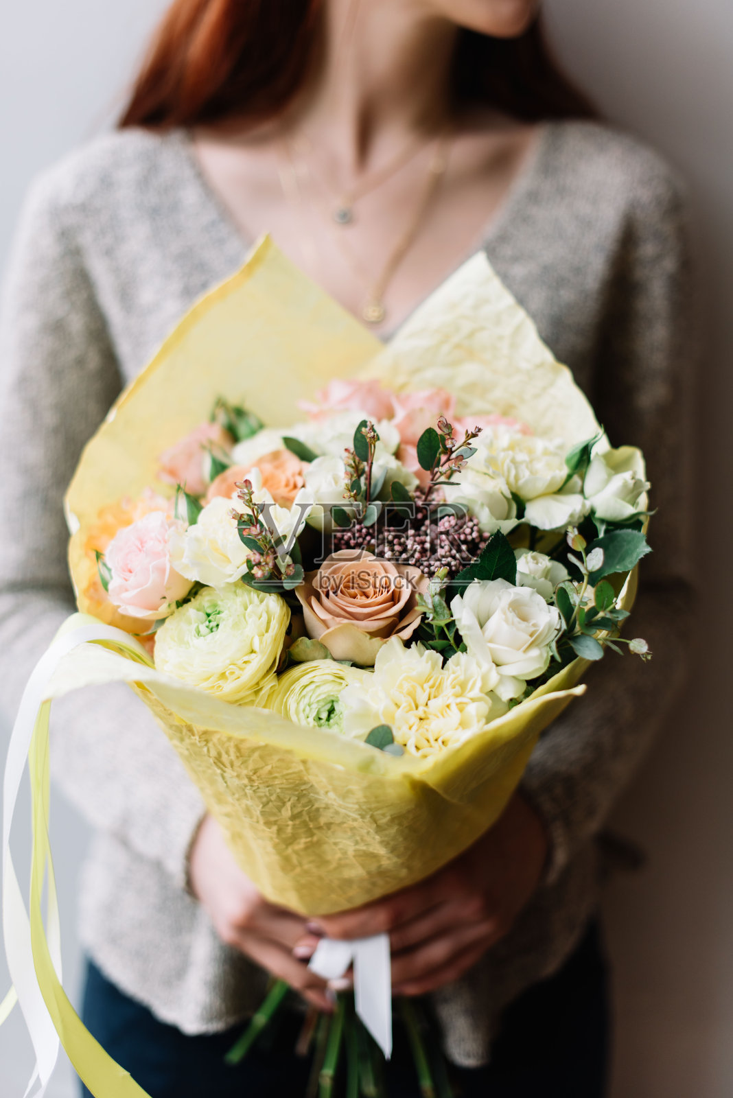 非常漂亮的年轻女子捧着一朵朵新鲜的毛茛、玫瑰、康乃馨、桉树花束，在灰色的墙壁背景上，有淡粉色和柠檬黄的颜色照片摄影图片