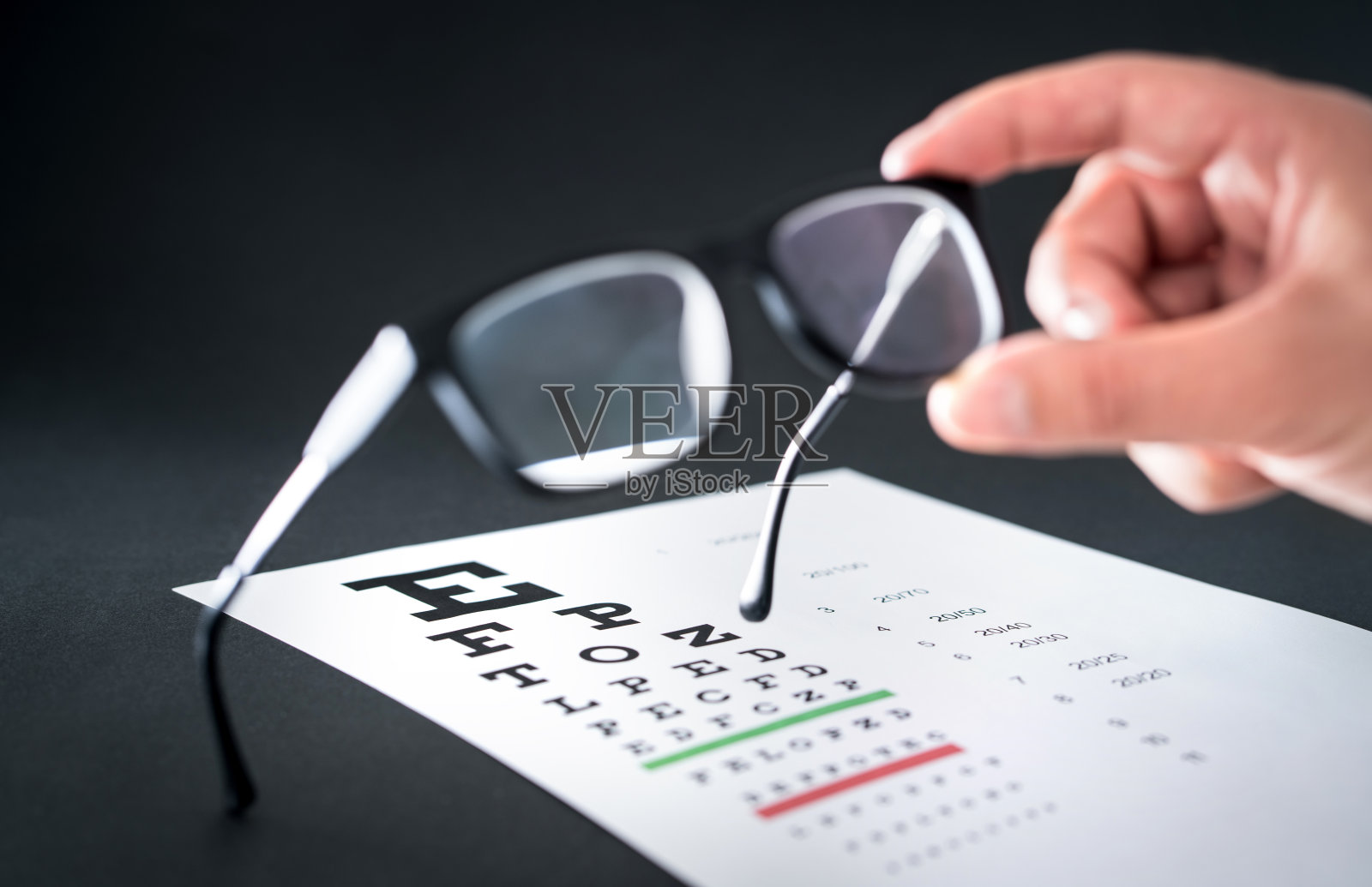 眼镜商拿着眼镜。背景中的视力测试表。眼科医生修理和修理眼镜或镜片。照片摄影图片