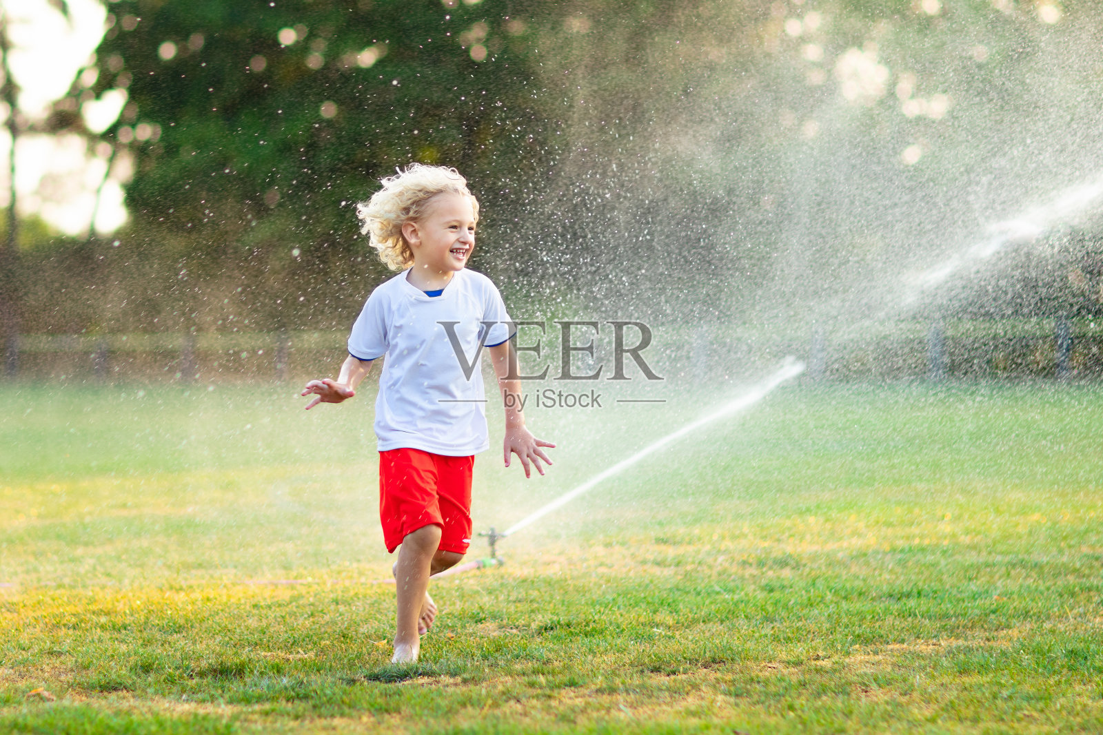孩子们玩水。孩子与花园洒水喷头。照片摄影图片