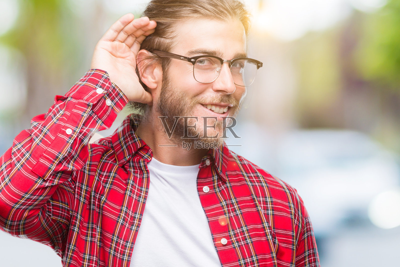 年轻英俊的男子长头发戴眼镜越过孤立的背景微笑与手捂耳朵听一听谣言或八卦。耳聋的概念。照片摄影图片