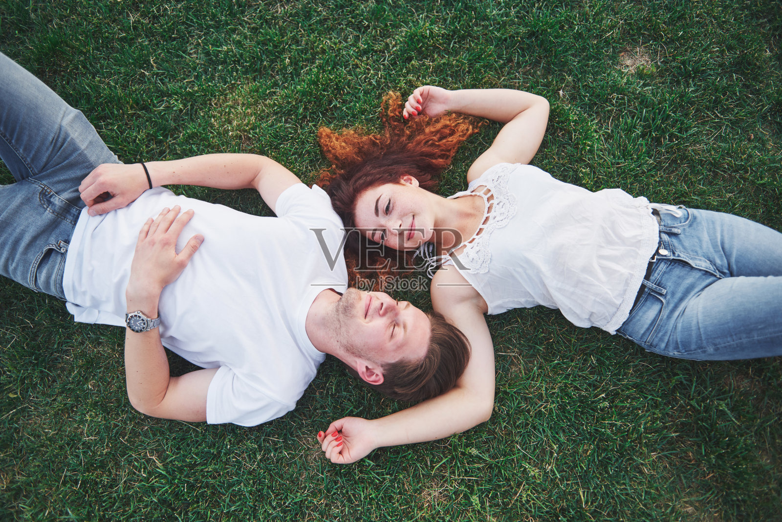 一对浪漫的年轻人躺在公园的草地上。他们看起来高兴。从以上观点。照片摄影图片