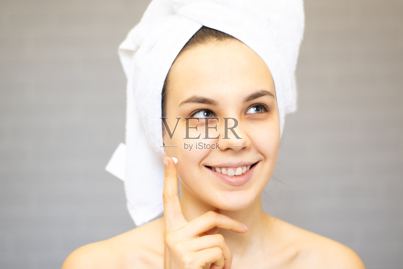 迷人的年轻女子包裹浴巾，在浴室淋浴后在她的脸上涂抹霜照片摄影图片
