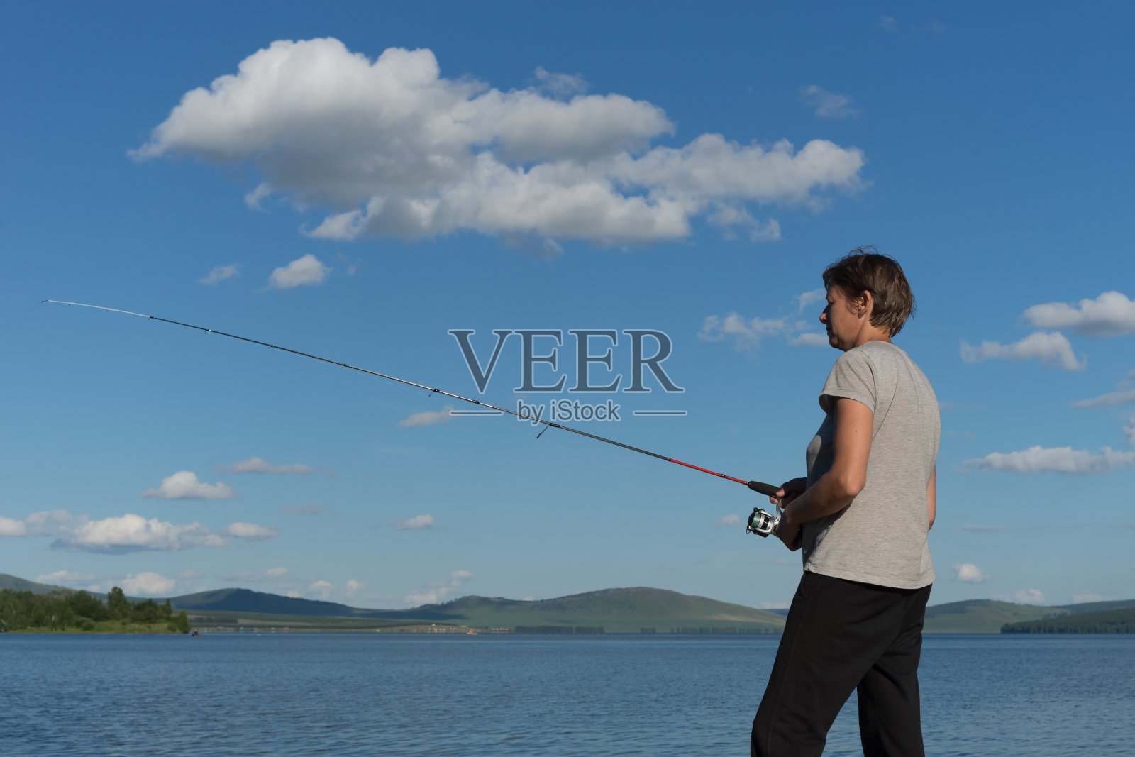 在蓝天白云的映衬下，一个女渔夫在一个蓝色的湖里捉到了一条鱼。照片摄影图片
