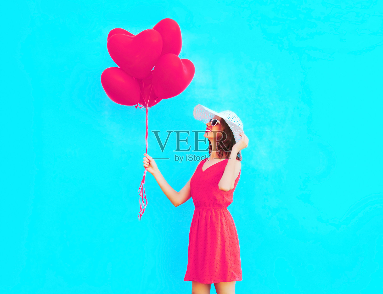 快乐的女人拿着蓝色背景上粉红色的心形气球照片摄影图片