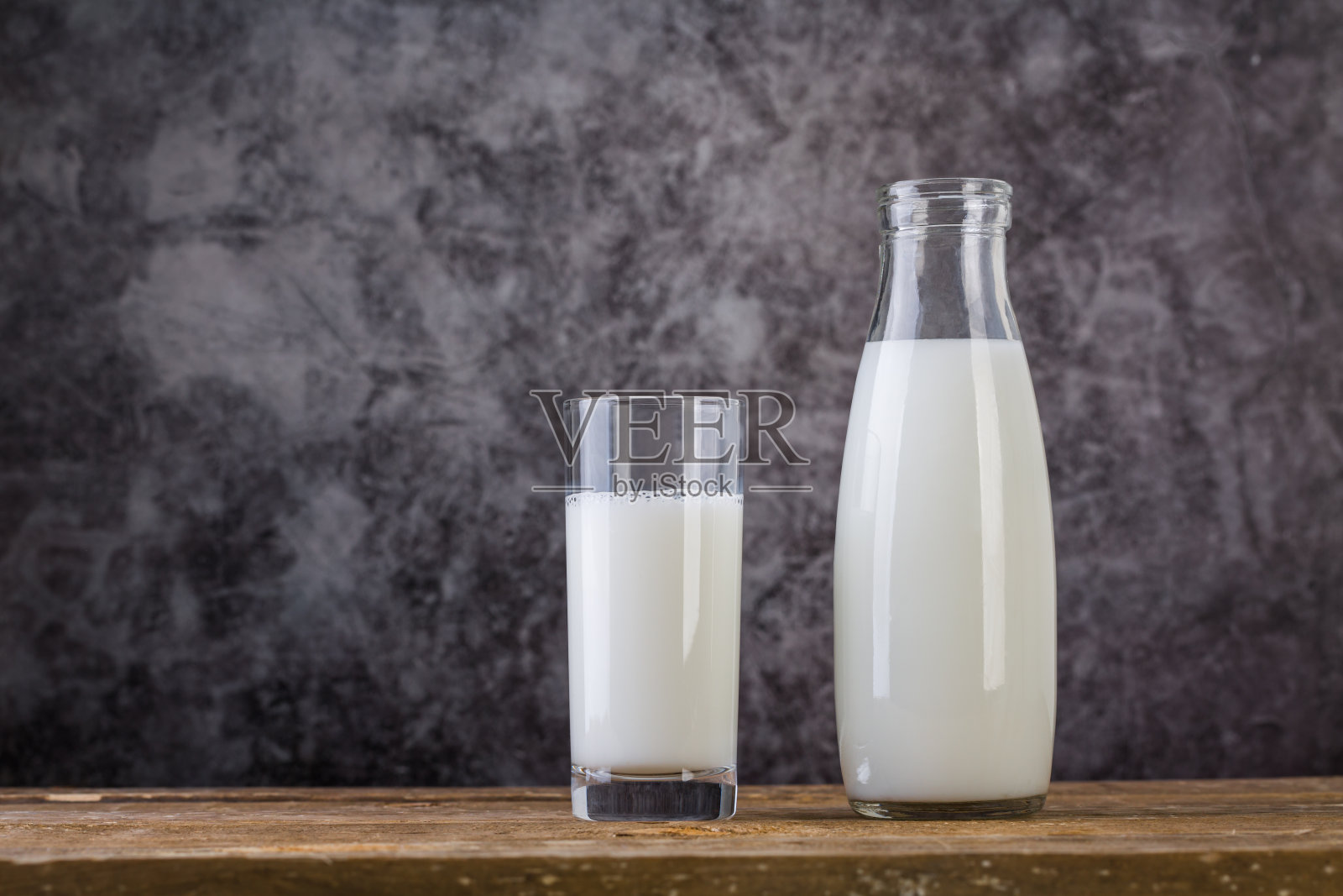 一瓶牛奶和一杯牛奶放在木桌上。照片摄影图片
