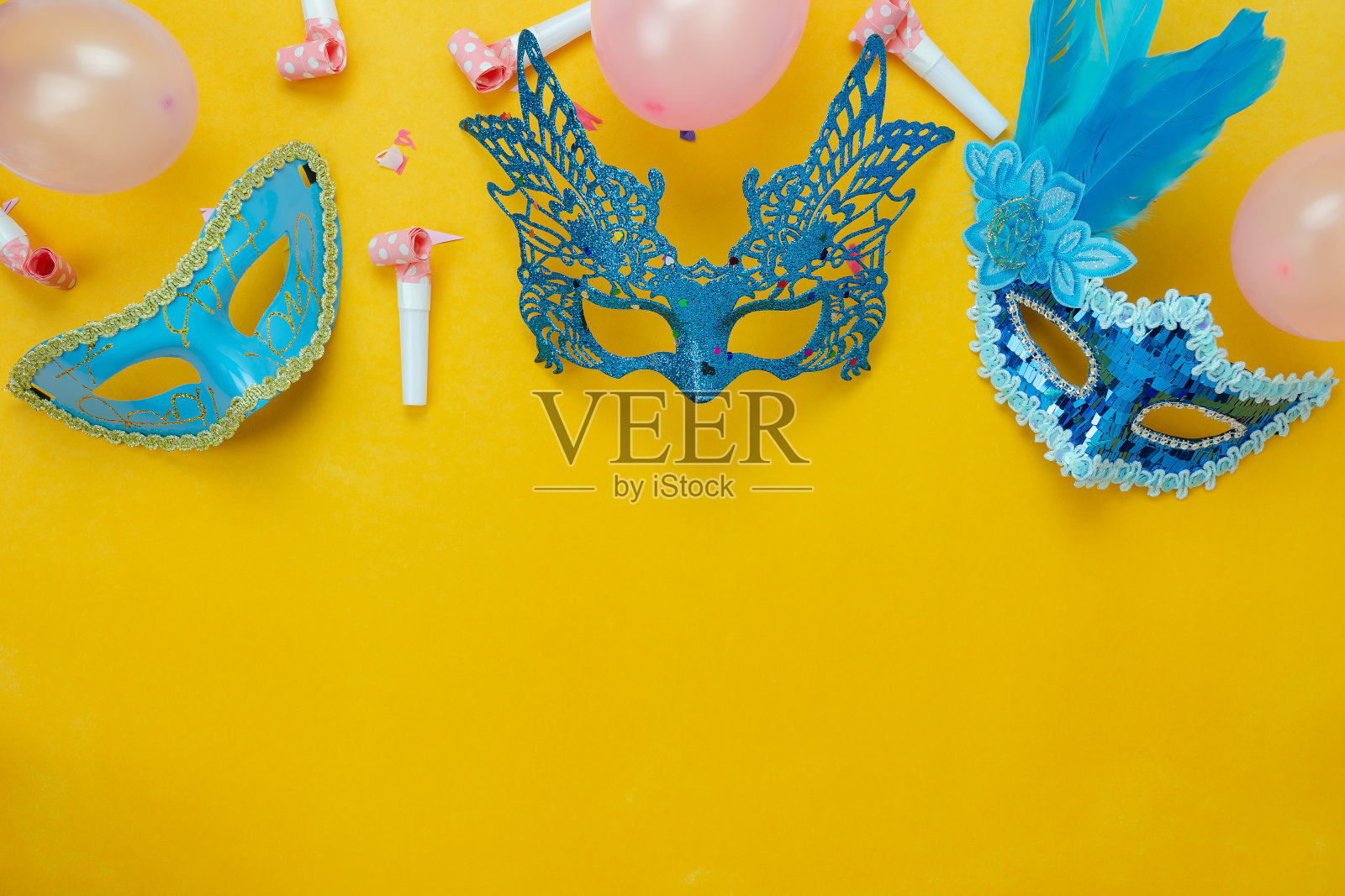 桌面俯瞰航拍图像的美丽多彩的狂欢节季节或照片亭prop Mardi Gras背景。平铺物体蓝色面具装饰和五彩纸屑和粉色气球在黄色墙纸。照片摄影图片