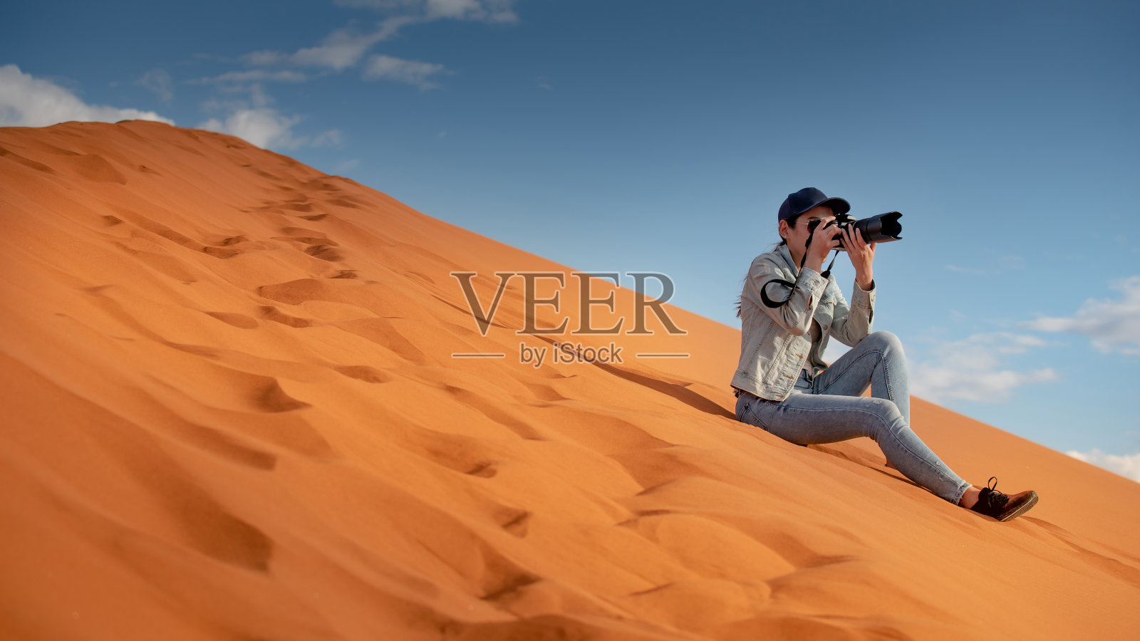 年轻的亚洲女性旅行者和摄影师拿着相机拍照，而坐在沙丘上的纳米比亚沙漠，非洲。旅行摄影的概念照片摄影图片