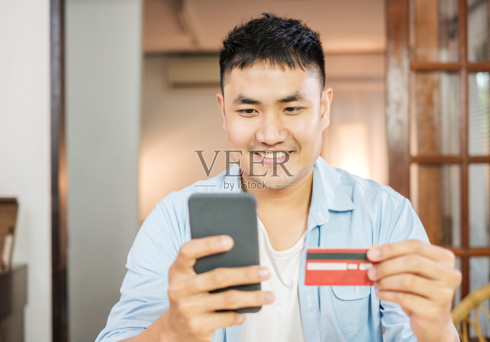 亚洲男子在家里用信用卡和手机在线购物。数码生活与科技。照片摄影图片