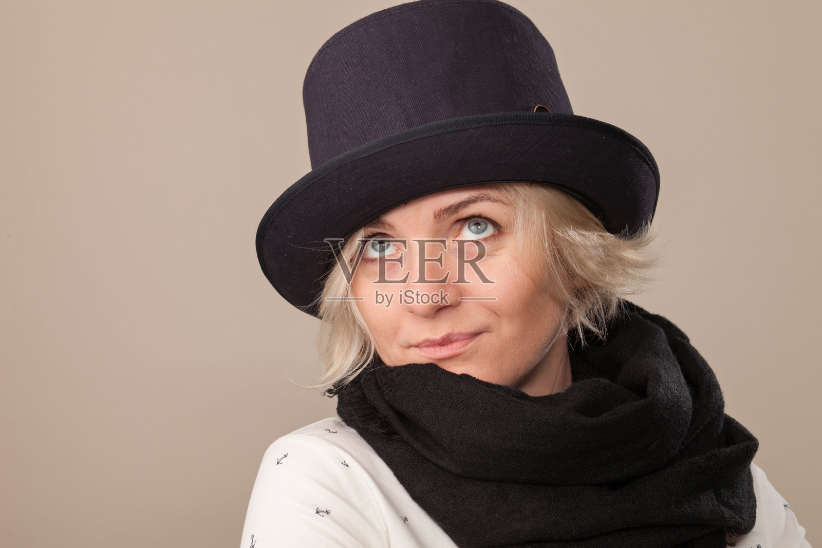一个迷人的40岁金发女人的工作室肖像在米色的背景上戴着帽子和黑色围巾照片摄影图片