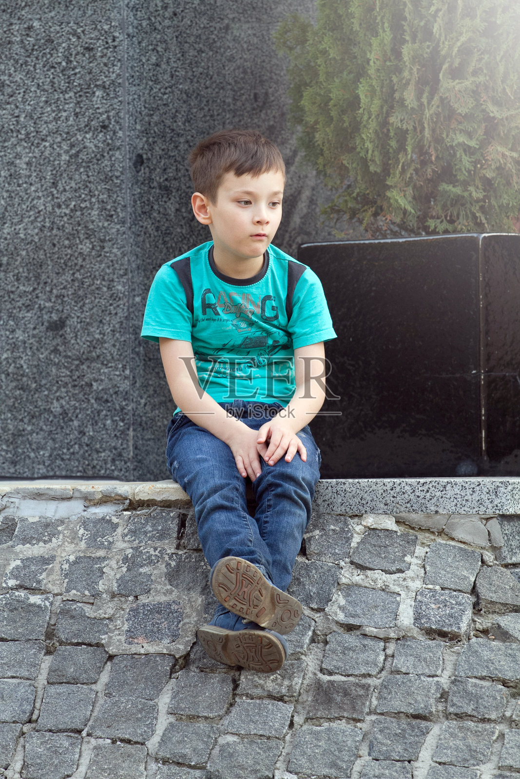 坐在户外地上的男孩。孤独或悲伤的概念。悲伤的小男孩照片摄影图片