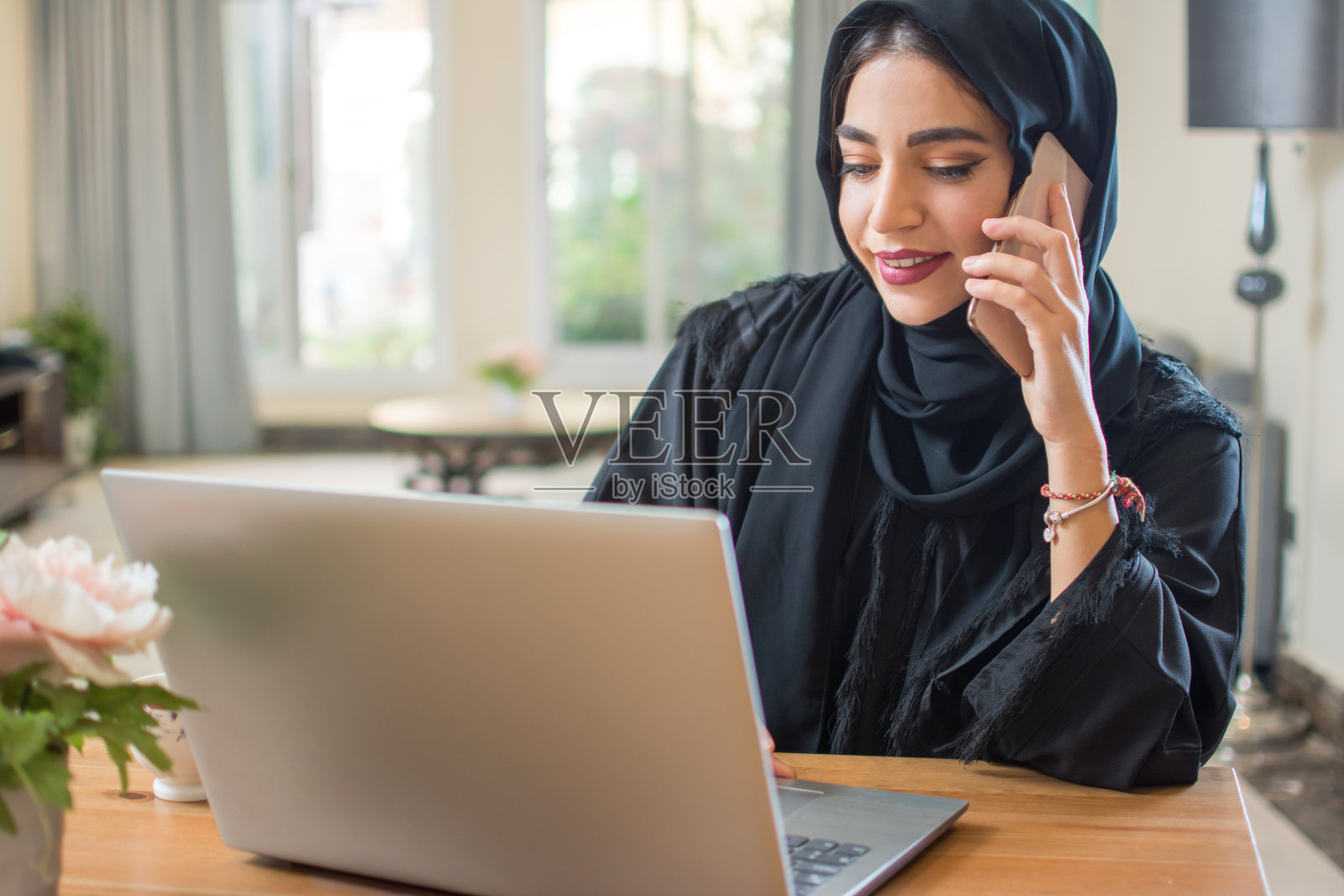 年轻漂亮的中东阿拉伯妇女在家里用手机和笔记本电脑聊天照片摄影图片