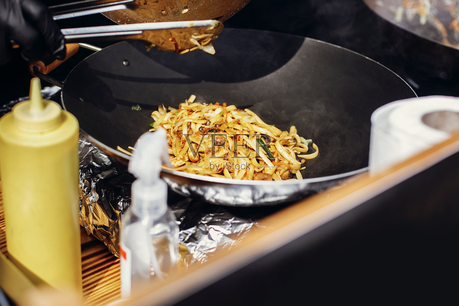 亚洲街头美食节。厨师在火上用平底锅煮面条和蔬菜。用明火在锅里炒日式蔬菜和虾面照片摄影图片