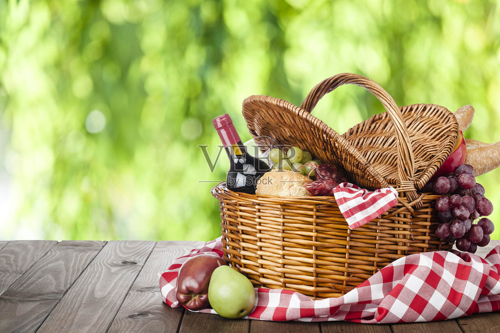 木桌子上的野餐篮子，映衬着稀疏的葱郁树叶照片摄影图片