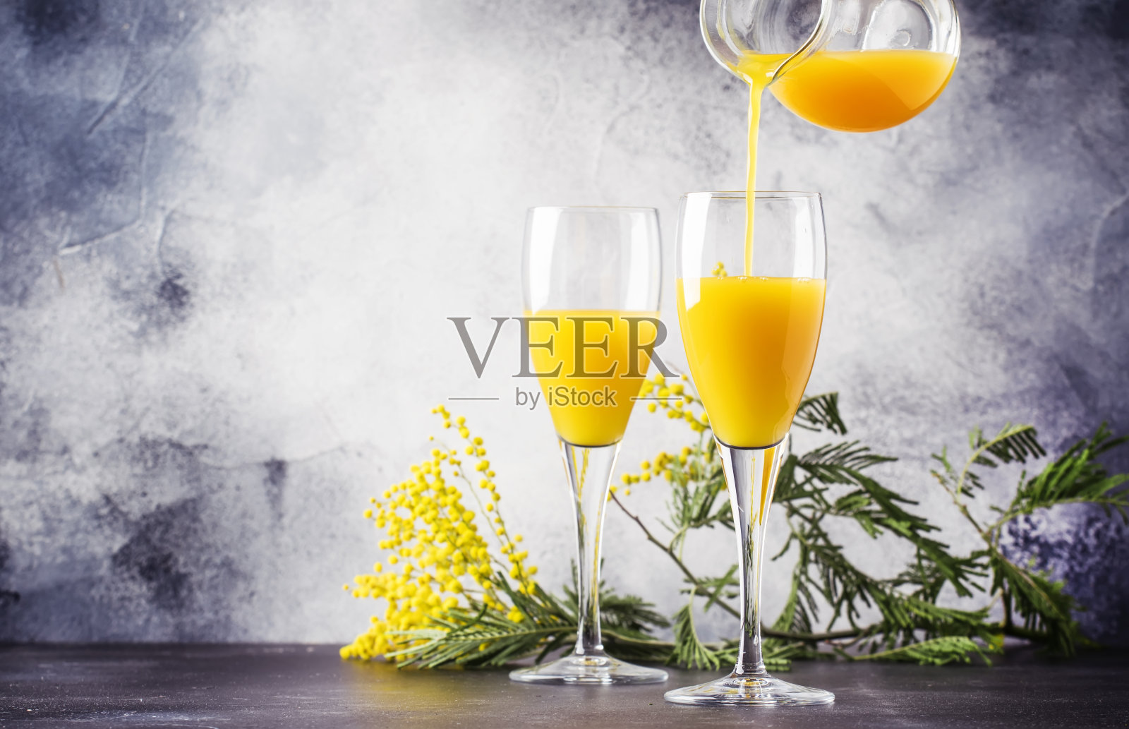 节日酒精鸡尾酒含苞欲放与橙汁和冷干香槟或起泡酒在玻璃杯，灰色的吧台与花，文字的地方，选择性焦点照片摄影图片