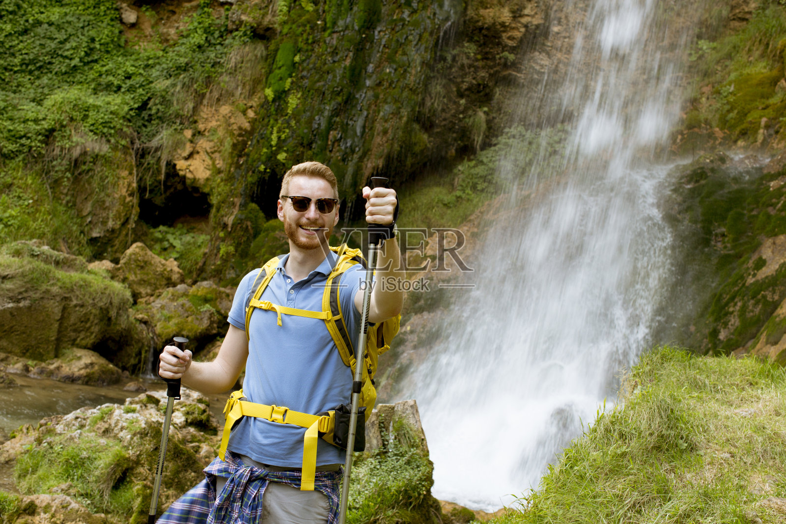 一个年轻的徒步旅行者在山上的瀑布旁停下来休息照片摄影图片