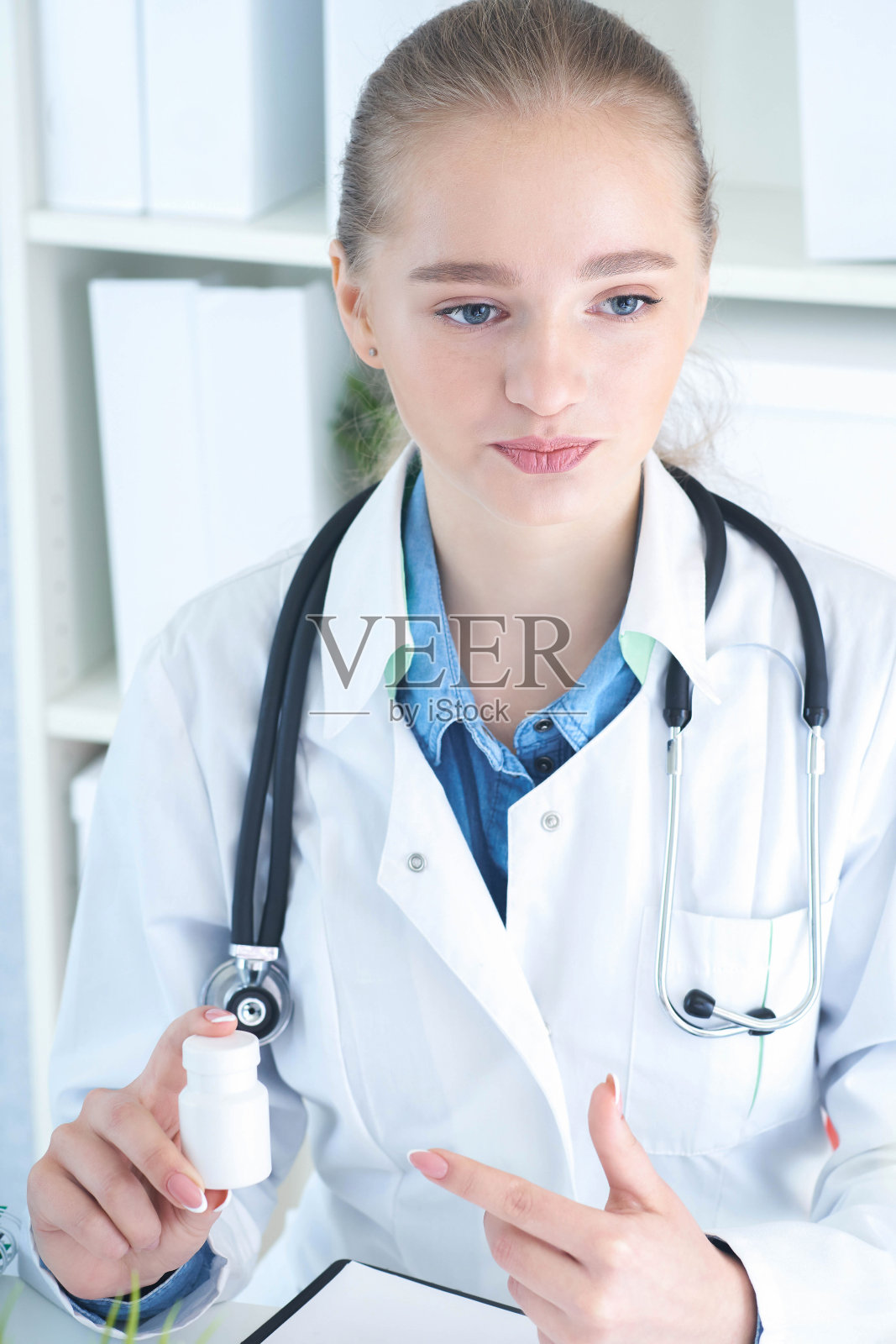 年轻的女医生抱着药瓶，并把它提供给来访者。抗抑郁药或维生素，健康生活。照片摄影图片